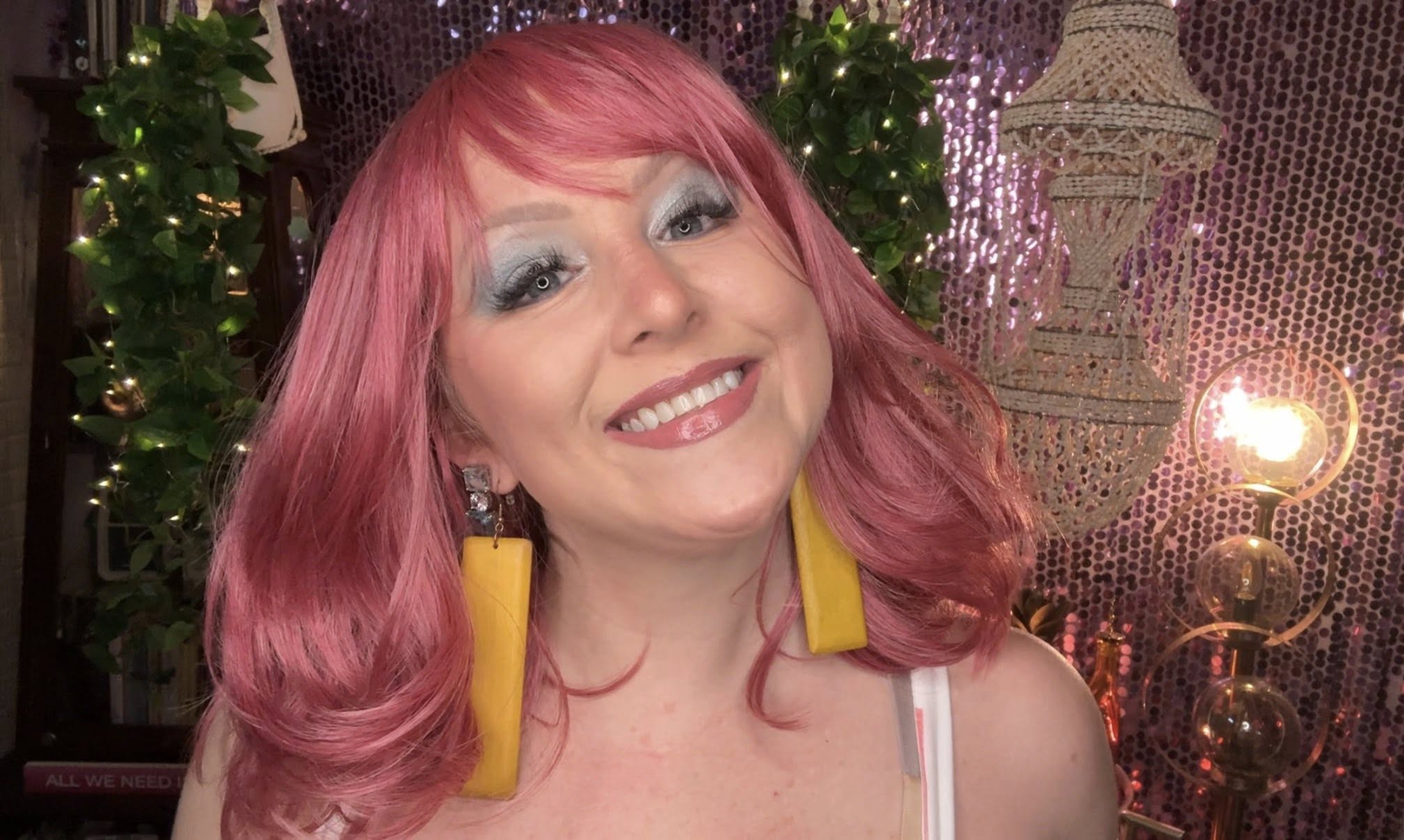 Breast cancer survivor Kelsey smiling radiantly in a form-fitting geometric patterned dress with a white base, posing confidently in front of a pink sequin backdrop before a breast cancer benefit.